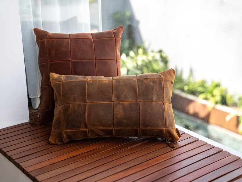 May include: Two brown leather pillows with a quilted design. The pillows are on a wooden surface.