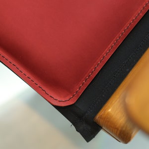 May include: Close-up of a red leather chair seat with black stitching and a wooden frame.