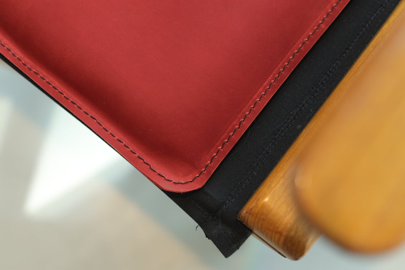 May include: Close-up of a red leather chair seat with black stitching and a wooden frame.