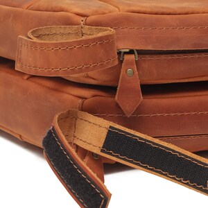 K&ouml;nnte beinhalten: Eine braune Ledertasche mit Rei&szlig;verschluss und einem schwarzen Gurt mit Klettverschluss.