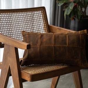 May include: A brown leather pillow with a quilted design sits on a wooden chair with a woven cane seat and back.