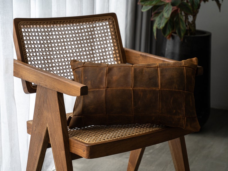 May include: A brown leather pillow with a quilted design sits on a wooden chair with a woven cane seat and back.