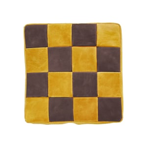 May include: Square cushion with a checkerboard pattern. The cushion features alternating squares of mustard yellow and dark brown. The edges are finished with a matching yellow trim. The cushion is made of a soft, plush material.