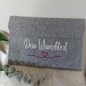 Könnte beinhalten: Eine rechteckige Dokumenten- oder Laptoptasche aus grauem Filz mit Klappverschluss. Auf der Vorderseite befindet sich der weiße Schriftzug "Dein Wunschtext" in Schreibschrift, platziert über einer magentafarbenen Grafik eines Herzens.