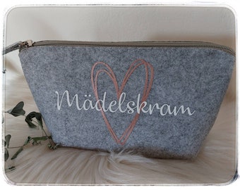 Peut inclure: Une trousse de toilette en feutre gris avec une fermeture éclair. La trousse a un motif de cœur rose doré et le texte "MädelsKram" en blanc.