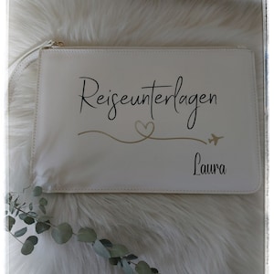 Könnte beinhalten: Weiße Reise-Clutch mit dem Text "Reiseunterlagen" und einem Herz- und Flugzeug-Design. Der Name "Laura" steht unter dem Design.