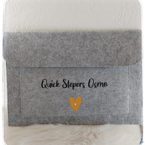 Könnte beinhalten: Graue Filz-Laptoptasche mit einem gelben Herzen und dem Text "Quick Stepers Osmo" in Schwarz.