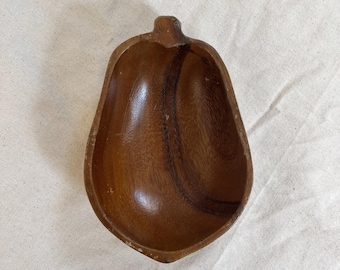 May include: A small, pear-shaped wooden bowl with a stem-like handle. The bowl is made of a dark brown wood with visible grain patterns. The interior is smooth and polished, while the exterior shows slight wear.