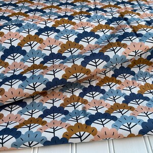 May include: Fabric with a repeating pattern of stylized fan-shaped designs in navy blue, light blue, tan, and blush pink on a white background. The fabric is folded, showing the texture and drape of the material.
