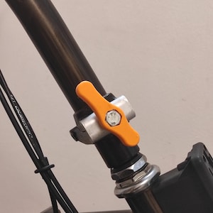 May include: A bicycle handlebar stem featuring a bright orange quick-release lever attached to a silver metal clamp. The assembly is secured with a central steel bolt marked with the number 8.8, mounted on a black cylindrical steering column.