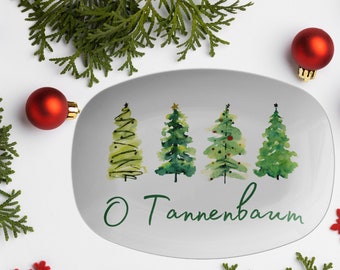 May include: An oval serving platter with a watercolor design of four Christmas trees in varying shades of green. The words "O Tannenbaum" are written in green script. Red ornaments, snowflakes, and greenery surround the platter.