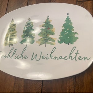 May include: White oval serving platter with a watercolor design of four Christmas trees in varying shades of green. The words "Fr&ouml;hliche Weihnachten" are written in green script below the trees.