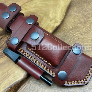 May include: A brown leather sheath with a fire starter and multiple snap closures. The sheath has a stitched design and is made of high-quality leather.