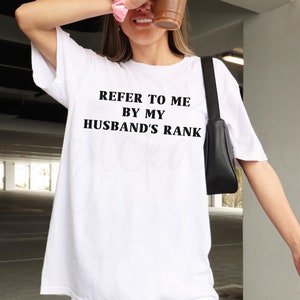 May include: White t-shirt with the text "REFER TO ME BY MY HUSBAND'S RANK" printed in black.