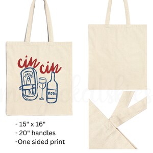 A natural colored cotton canvas tote bag. Design large in center of bag. Design says cin cin in fancy print in deep bright red all lowercase and curved on top of elements below. Elements pictured are thick sketched doodles of tinned sardines and a rose bottle with a wine glass in the center of both elements. Elements color is in bright coastal blue. Elements have a slight distressed look to them. For the fisherman aesthetic, Italian and mediterranean summer aesthetic, and sardine lovers.