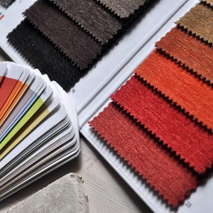 May include: A close-up of fabric swatches in various shades of brown, orange, and red. The swatches are arranged in a fan-like pattern on a white surface. A color palette with a variety of shades of yellow, orange, and red is also visible in the image.