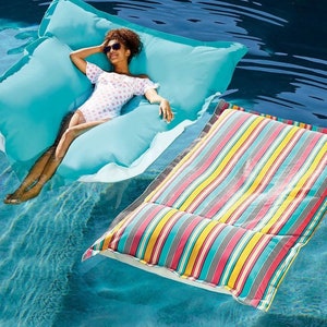 May include: A person wearing sunglasses and a polka dot swimsuit relaxes on a large, turquoise pool float. A second, striped pool float is nearby. The water is a deep blue, creating a relaxing summer scene.
