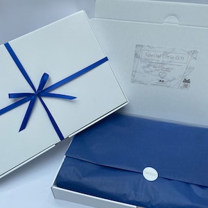 May include: A white gift box with a blue ribbon and bow. The box is open and inside is blue tissue paper. The box has a label that says "Special Little Gift Co. Unique and Thoughtful Presents for Special Occasions Made with Love and Care Just For You"