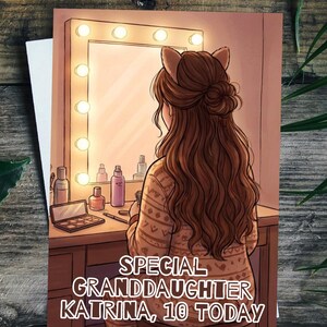 May include: A greeting card illustration depicts a young girl with brown hair and cat ears, seated at a vanity with a lighted mirror. The text reads "SPECIAL GRANDDAUGHTER KATRINA, 10 TODAY". The card is on a wooden surface.
