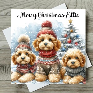 May include: Christmas card with three dogs in winter attire, set against a snowy backdrop and a Christmas tree. The card says "Merry Christmas Ellie". The dogs wear hats and sweaters.
