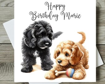 May include: A birthday card featuring two adorable puppy illustrations. One is black, the other is tan, and is holding a bone-shaped toy. The card reads "Happy Birthday Marie" in elegant script.