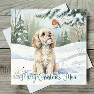 May include: A Christmas card with a watercolour illustration of a dog in a snowy scene. A small bird sits on a branch above the dog. The card has the text "Merry Christmas Mum" in teal script.