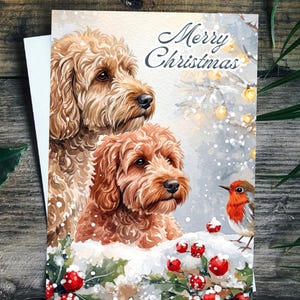 May include: A rectangular Christmas greeting card featuring a watercolour illustration of two curly-haired golden-brown dogs sitting in snow. A small robin sits near red holly berries in the foreground. The text Merry Christmas is printed in black.