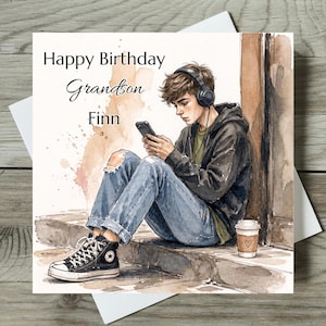 May include: A square birthday greeting card featuring a watercolor illustration of a young person wearing a black hoodie, blue ripped jeans, and black high-top sneakers. The person wears headphones and uses a smartphone. Text reads: Happy Birthday Grandson Finn.