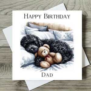 May include: A birthday card featuring a black dog with a teddy bear in a bed. The card says "Happy Birthday Dad".