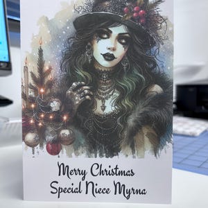 K&ouml;nnte beinhalten: Weihnachtskarte mit einer Aquarellillustration einer Frau mit schwarzem Zylinder und Schmuck. Die Karte hat ein Weihnachtsthema mit einem kleinen Weihnachtsbaum und dem Text "Merry Christmas Special Niece Myrna".