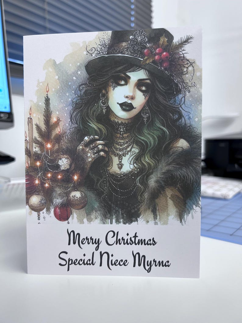 K&ouml;nnte beinhalten: Weihnachtskarte mit einer Aquarellillustration einer Frau mit schwarzem Zylinder und Schmuck. Die Karte hat ein Weihnachtsthema mit einem kleinen Weihnachtsbaum und dem Text "Merry Christmas Special Niece Myrna".