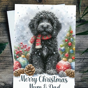 May include: A Christmas card with a black dog wearing a red and green scarf, set in a snowy scene with baubles and pine cones. The card says "Merry Christmas Mum & Dad".