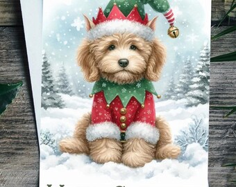 May include: Christmas card featuring a fluffy, light brown dog dressed as an elf in a red and green outfit, with a matching hat and bell. The card has the words "MERRY CHRISTMAS" and is set against a snowy winter scene.
