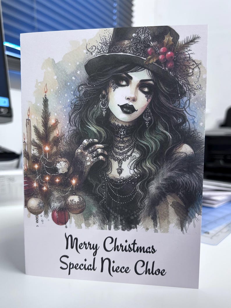 K&ouml;nnte beinhalten: Weihnachtskarte mit einer gotischen Illustration einer Frau mit Zylinder, langen dunklen Haaren und aufwendigem Schmuck. Links ein kleiner Weihnachtsbaum mit Kugeln und Kerzen. Der Text lautet "Merry Christmas Special Niece Chloe."
