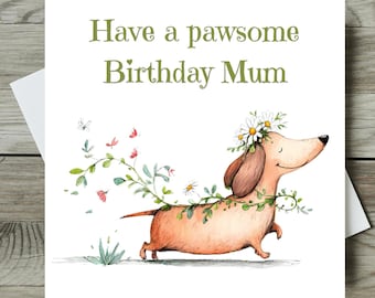 May include: A greeting card with the text "Have a pawsome Birthday Mum." The card features a watercolor illustration of a dachshund wearing a flower crown and garland. Butterflies and floral elements surround the dog.