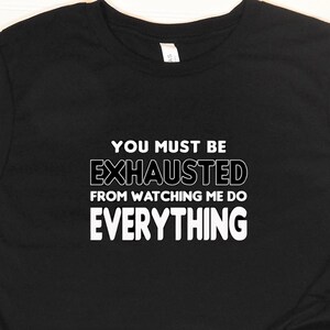 May include: Black t-shirt with white text that reads "You must be exhausted from watching me do everything."