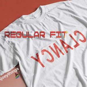 Op de afbeelding: Wit T-shirt met rode tekst die "REGULAR FIT" en "CIAYNCY" in omgekeerde volgorde luidt. De tekst is licht beschadigd.