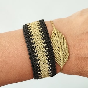 May include: A wide black and gold macrame bracelet with a geometric pattern alongside a thin gold cord bracelet featuring a central leaf-shaped macrame charm. Both pieces are crafted from woven thread and sit side by side on the wrist.