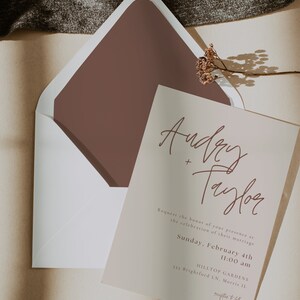 May include: A wedding invitation with a light brown background and a brown envelope. The invitation features the names "Audrey + Taylor" in a handwritten script font. The text reads "Request the honor of your presence at the celebration of their marriage. Sunday, February 4th 11:00 am HILLTOP GARDENS 333 Brightford LN, Morris IL reception to follow"