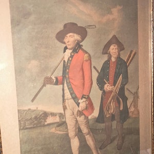 May include: An antique print of two men playing golf. The man on the left is wearing a red coat and a tricorne hat. The man on the right is wearing a blue coat and a hat. The print is titled "To the Society of Golfers at Blackheath."