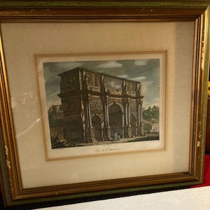 May include: A framed print of an antique illustration of the Arch of Constantine in Rome, Italy. The print is in black and white with a sepia tone and features a detailed depiction of the arch.
