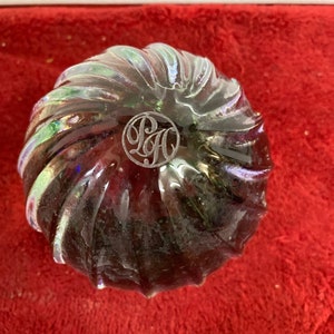 May include: A clear glass paperweight with a swirling pattern and iridescent finish. The paperweight has a circular engraved logo that reads "P&H".