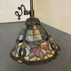 May include: A stained glass pendant light with a black metal frame and a floral design. The glass is multi-colored and features shades of blue, green, pink, and yellow.