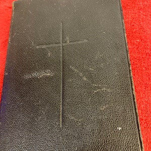 Könnte beinhalten: Ein schwarzes, ledergebundenes Buch mit einem geprägten Kreuz auf dem Einband.