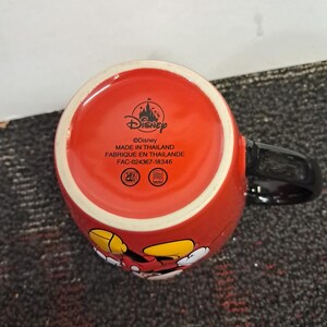 May include: Red ceramic mug featuring Mickey Mouse. The mug has a black handle and the text "&copy;Disney MADE IN THAILAND FABRIQUE EN THAILANDE FAC-024367-18346" printed on the bottom. The mug has a glossy finish.