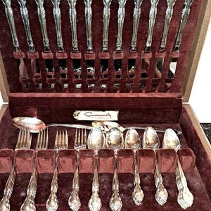 May include: A silver Community silverware set in a brown velvet-lined case. The set includes knives, forks, and spoons with ornate handles. The case is open, revealing the neatly arranged utensils.