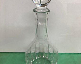 May include: A clear glass decanter with a textured, ribbed design and a clear glass stopper. The stopper has a rounded, bulbous top.