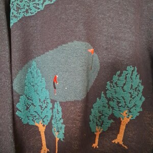 May include: Dark navy blue sweater with a golf course design. The sweater features a green golf course scene with a golfer in red, green trees, and a red flag. The trees have brown trunks and green foliage.