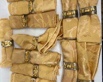 May include: A set of 15 gold and silver napkin rings with a floral design. The rings are placed on top of folded napkins with a similar floral pattern.
