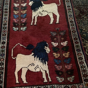 May include: A red rug with a traditional design featuring two white lions with black manes and floral motifs. The rug has a fringe border.